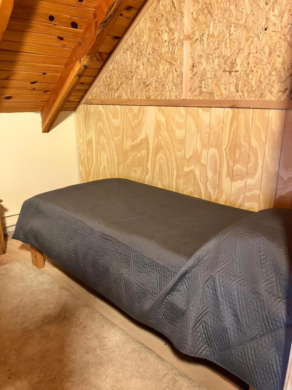 Cama individual con cubrecama gris junto a la pared de madera