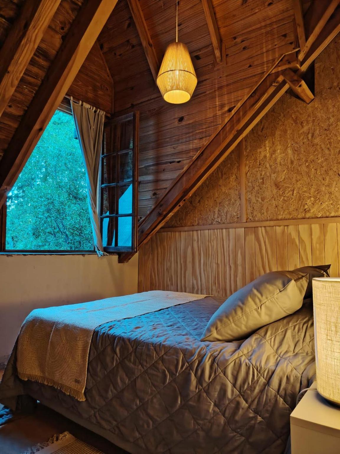 Cama doble junto a una ventana con vista a los árboles